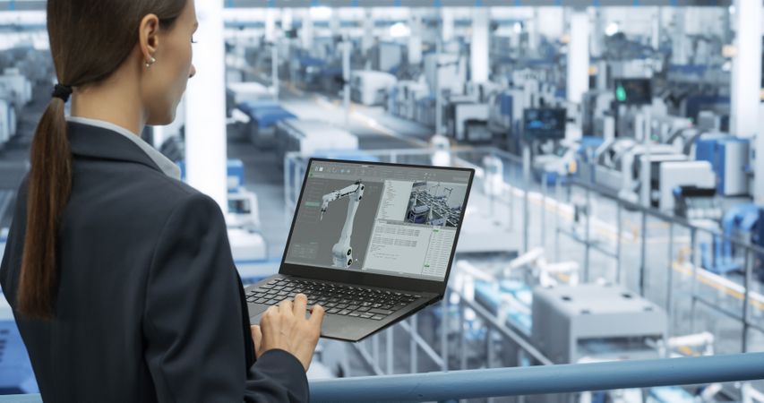 Electronics Manufacturing Technician Working on a Laptop Computer at a Factory Space. Female Specialist Developing, Maintaining, Upgrading Programs for Machine Production and Assembly