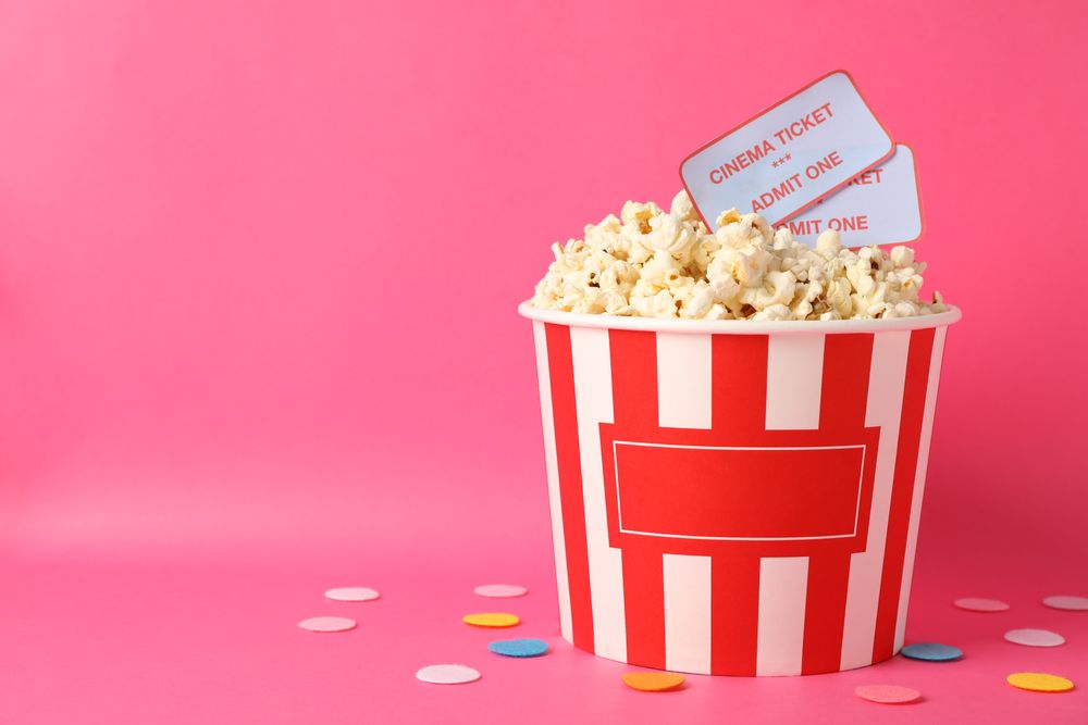 Confetti, bucket with popcorn and tickets on pink background, copy space