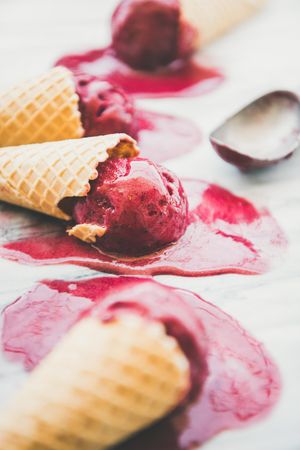 Cones of dark berry ice cream melting on marble slab, vertical composition, side view with scoop