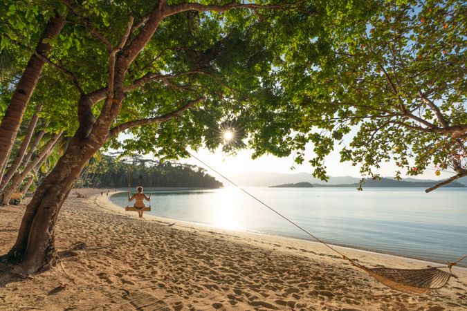 Female swinging on tranquil sandy beach