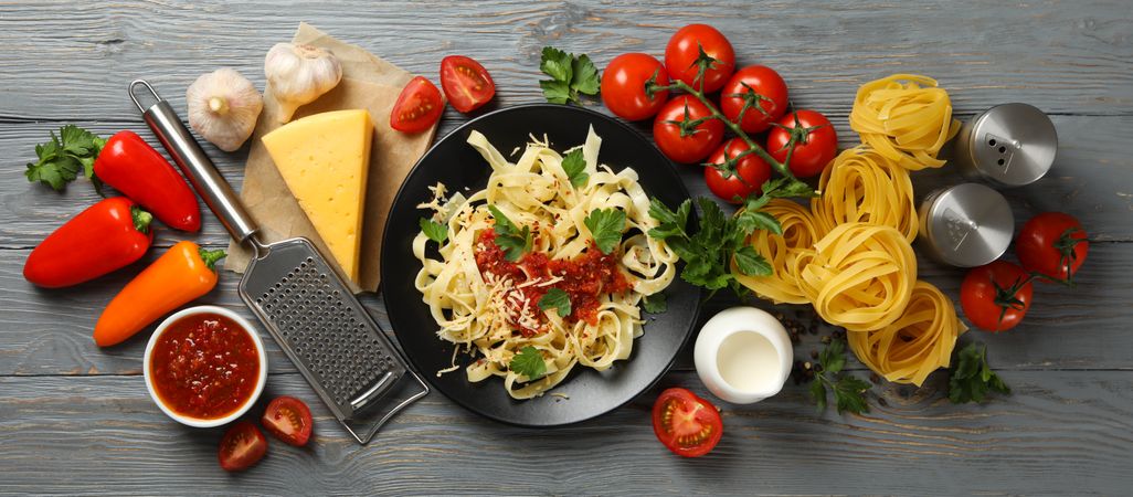 Composition with plate of tasty pasta and ingredients for cooking on wooden background