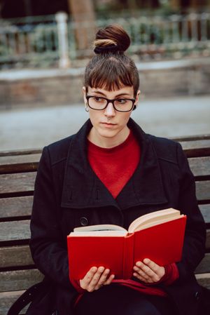Young woman reading book on bench in park