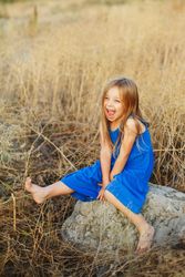 Female child dressed in blue sitting on bolder in field