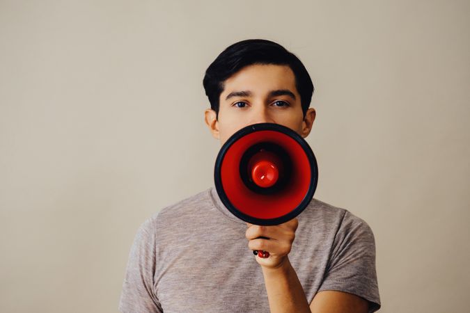 Hispanic male holding red loudspeaker to his face