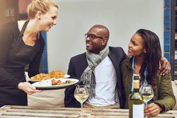 White waitress serving a Black couple dining al fresco