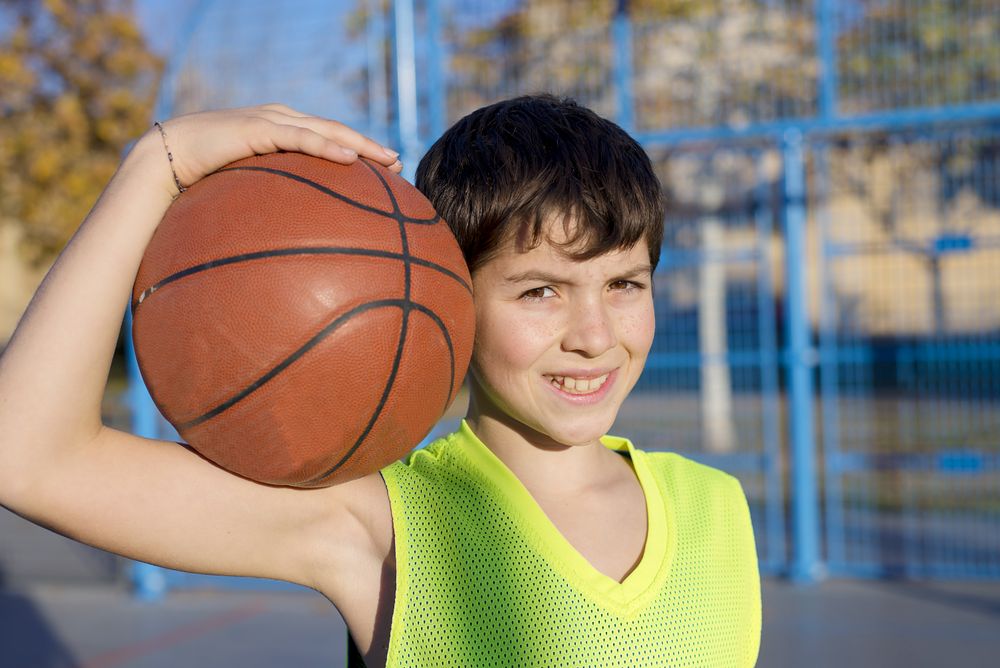 Young basketball player standing on the court wearing a yellow sleeveless and holding a basketball