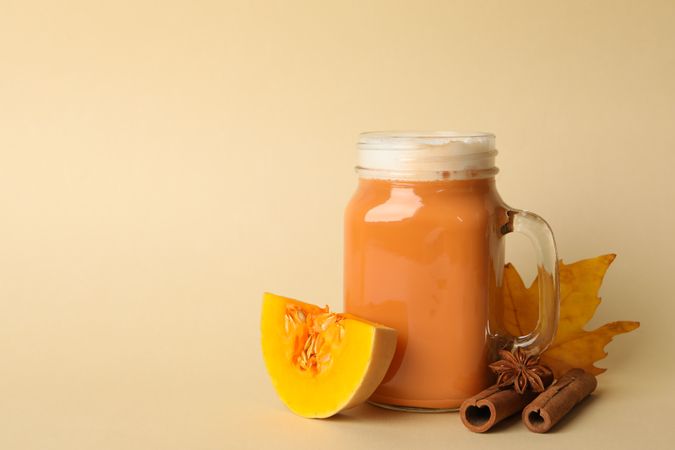 Composition with pumpkin latte, pumpkin, leaf and cinnamon on beige background