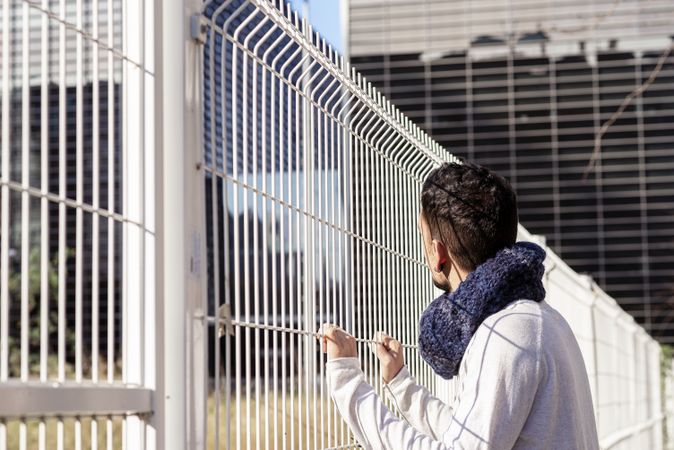 Man leaning on a metallic fence while looking up to the business buildings