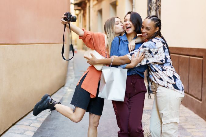 Three happy women in narrow lane taking selfie with camera