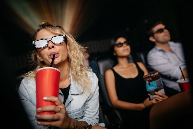 Young woman having cold drink wearing 3d glasses and watching movie in theater