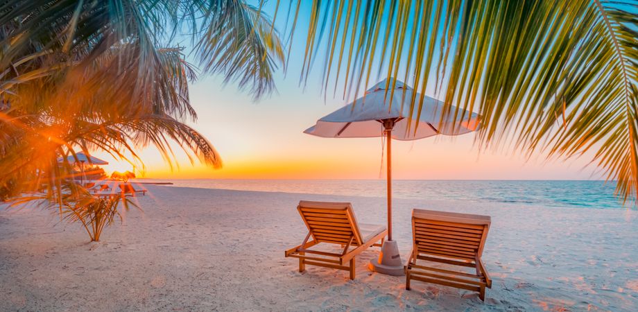 Wide angle of a beach at sunset with two chairs and umbrella