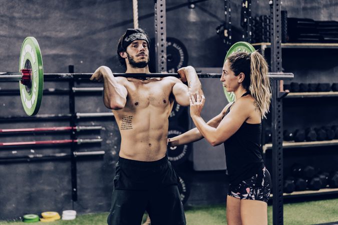 Muscular man lifting heavy weight in sport club and listening to personal trainer
