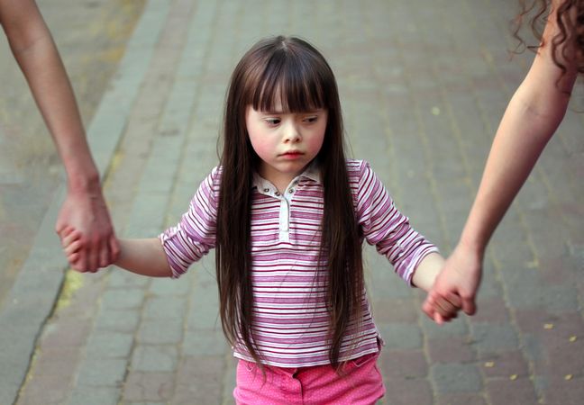 A girl holding the hands of two people outside