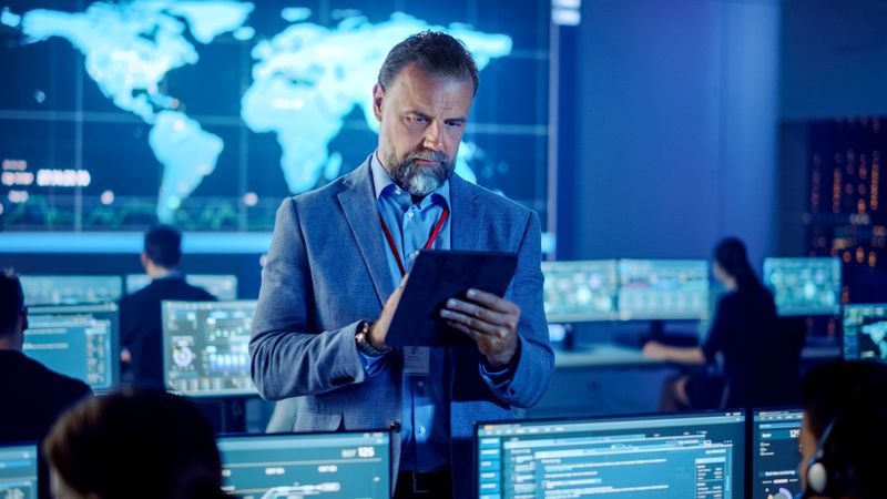 Focused Man Analyzes Data on a Tablet in a High-tech Control Room