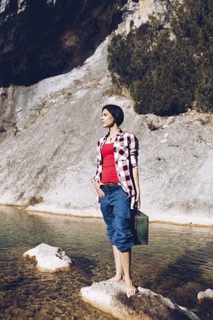 woman standing on rock with case near clear water in lake