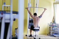 Tattooed male exercising his arms on pull down machine 4NGjmb