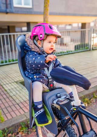 Portrait of little girl with pink helmet on sitting in bike seat ready for ride