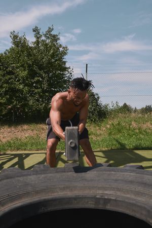 Muscular Black guy hammering tire in outdoor gym