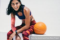 Happy fitness trainer relaxing and sitting next to basketball 0W8lx5