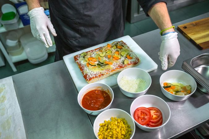 Anonymous male chef preparing vegetarian focaccia with healthy ingredients in a restaurant kitchen