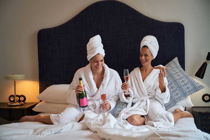 Happy women resting on bed with champagne and croissants