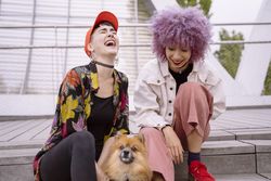 Women in colorful shirt and with pink hair training dog and having fun
