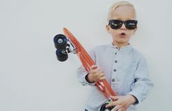 Young trendy blond boy leaning against a wall with red skateboard, copy space
