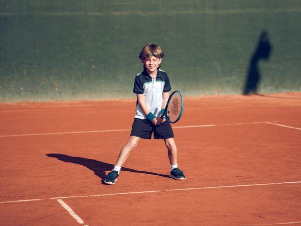 Happy child smiling while practicing tennis on clay court