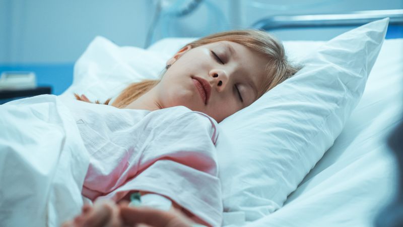 Recovering Little Girl Lying in the Hospital Bed Sleeping, Mother Holds Her Hand Comforting.