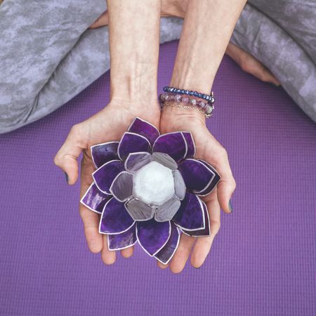 Top angle view of hands holding a purple glass lotus.  Yoga and meditation concept.