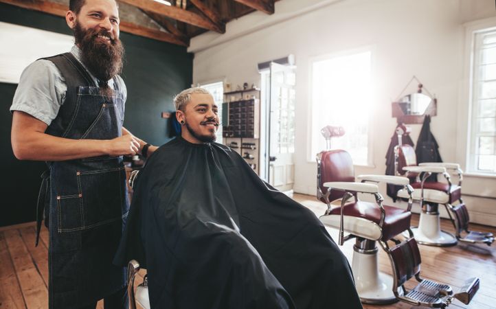 Hairstylist with client sitting at barbershop and smiling
