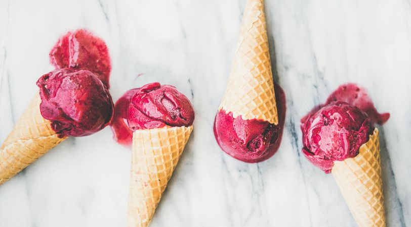 Four cones of dark berry ice cream on marble slab, horizontal composition