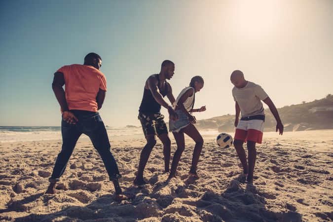 Group of friends playing soccer together on sandy beach in the afternoon