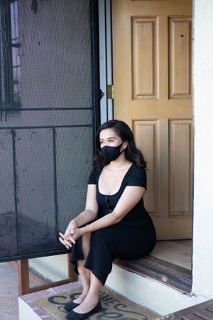 Beautiful woman with mask sitting on front steps of house looking out