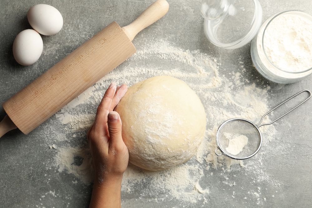 Female hand hold dough on gray background with ingredients for baking