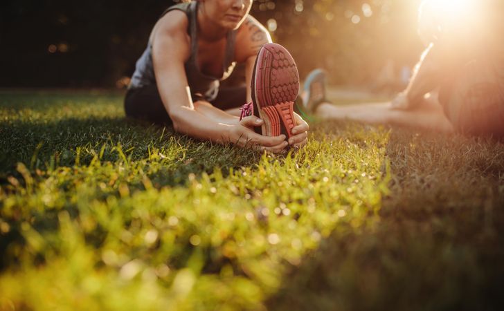 Cropped shot of woman sitting on grass and warming up for exercise