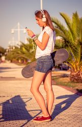 Young girl with skateboard and headphones listening music outdoors