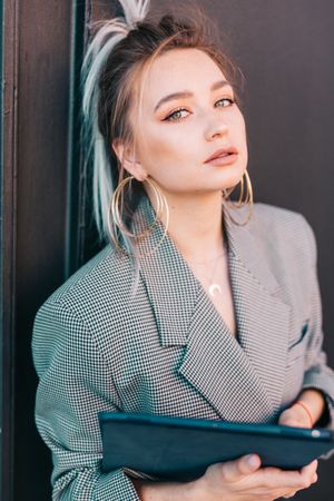 Stylish businesswoman with laptop leaning on wall