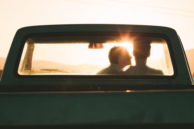 Rear view of couple sitting inside pick up truck facing sunset