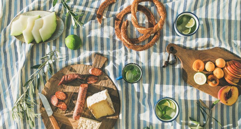 Summer picnic spread with pretzels, fruits, mojitos, meat and cheese board