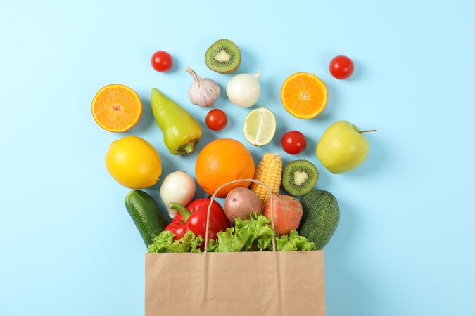 Flat lay with paper bag, vegetables and fruits on blue background, copy space