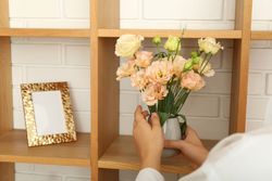 Woman put vase with flowers on shelf against brick wall background
