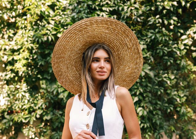 Portrait of woman in straw hat standing in front of a bush
