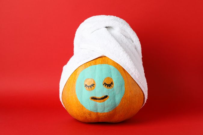 Pumpkin with facial mask and towel on red background, copy space