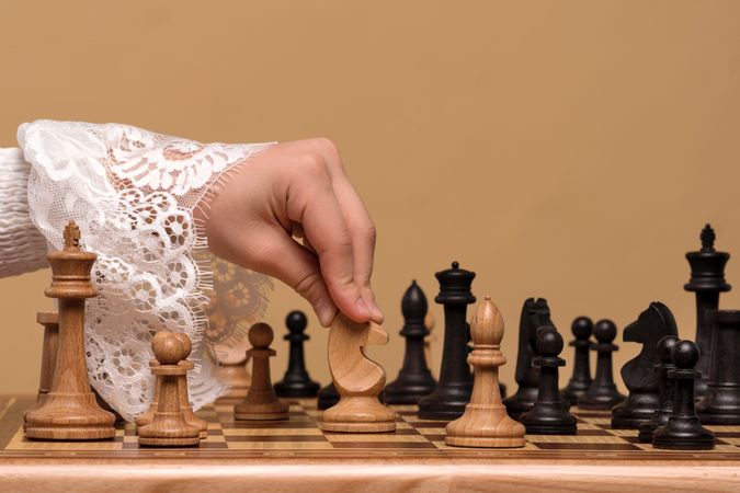 Hand in lace blouse moving chess piece on board.