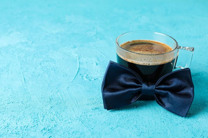 Blue bow tie and cup of coffee on color background, space for text