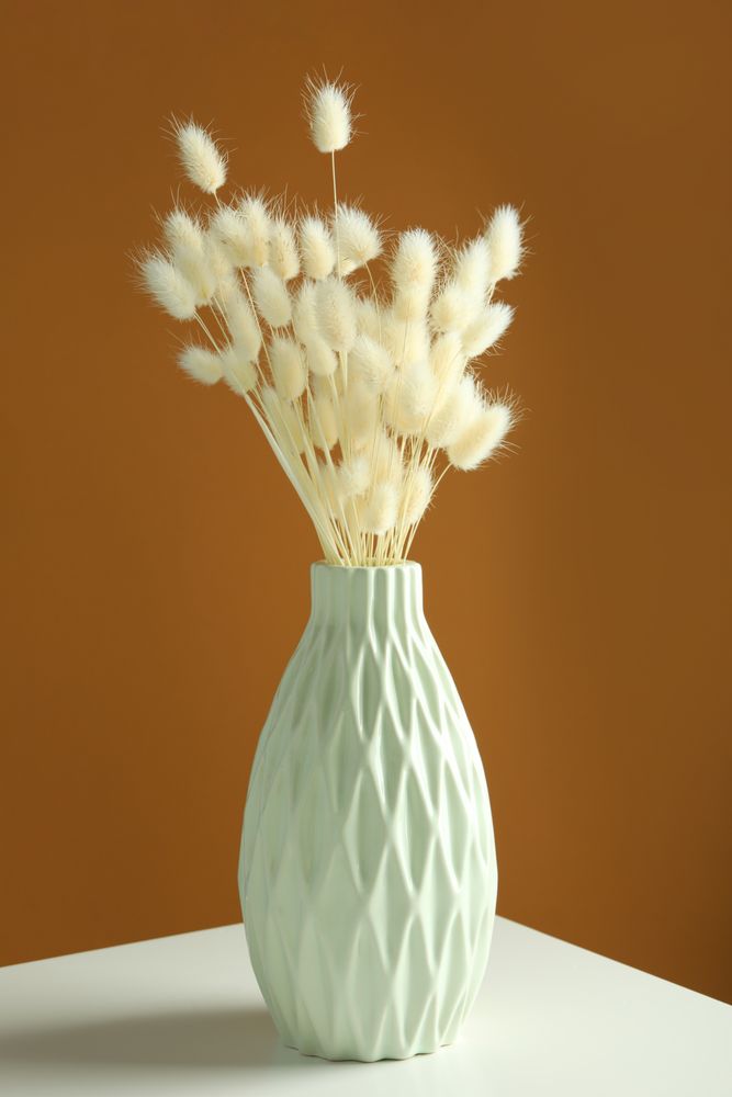 Mint green vase with dried bunny tail bouquet in brown room