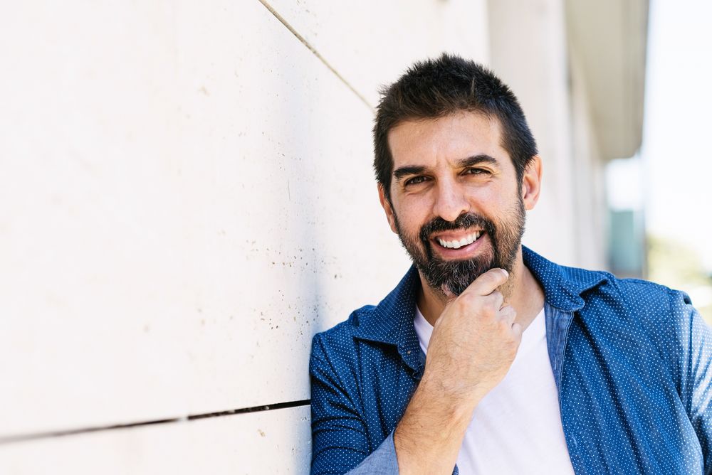 Happy Latino man in denim standing outside holding beard