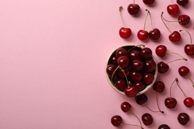 Ripe cherry fruits in a bowl on a pink background