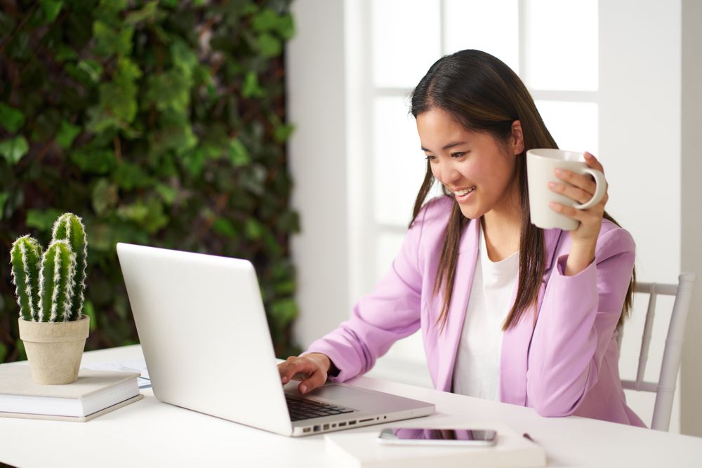 a young asian woman smiling working at the computer in the coworking space having coffee
